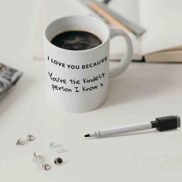 A white mug with black writing on a desk next to a black dry erase marker